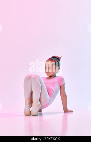 Porträt einer kleinen süßen Ballerina-Tänzerin, die Ballett-Badeanzug und pointe-Training vor der Vorstellung in gemischtem Neonlicht trägt. Stockfoto