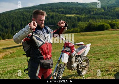 Ein professioneller Motocross-Fahrer in einem Vollanzug, Handschuhen und Rucksack bereitet sich auf ein waghalsiges Abenteuer durch den Wald vor, das auf einen vorbereitet ist Stockfoto