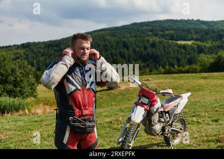 Ein professioneller Motocross-Fahrer in einem Vollanzug, Handschuhen und Rucksack bereitet sich auf ein waghalsiges Abenteuer durch den Wald vor, das auf einen vorbereitet ist Stockfoto