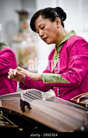 Eine Chinesin in traditionellem Gewand spielt Gu-Zheng, ein mit Fingern gerupftes Saiteninstrument. Stockfoto