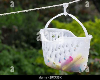 Nahaufnahme eines Plastikkorbs, der an einer Wäscheleine hängt, mit Wassertropfen Stockfoto