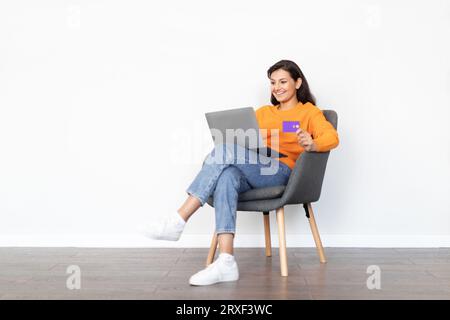 Fröhliche junge indische Frau mit Laptop, Kreditkarte, weißem Hintergrund Stockfoto