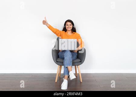 Positive indische Frau Digital Nomad mit Laptop und Kopfhörer Stockfoto
