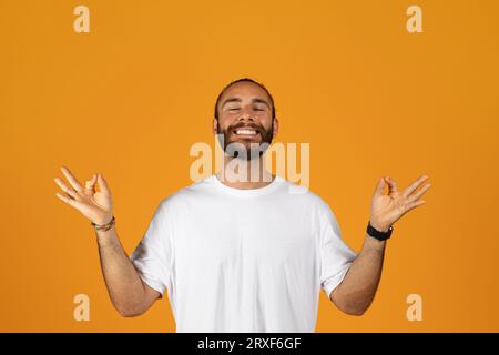 Froher, tausendjähriger kaukasischer Mann mit Bart im weißen T-Shirt meditiert, genießen Atemübungen Stockfoto