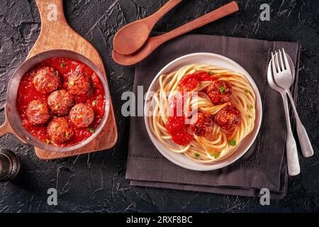 Fleischbällchen. Rindfleischbällchen, flach über dem Kopf liegend, in einer Pfanne und mit einem Teller Spaghetti-Pasta auf schwarzem Hintergrund Stockfoto