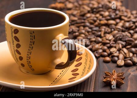 Gewürzsternanis, Tasse Kaffee und Untertasse aus nächster Nähe. Kaffeekörner auf dem Tisch. Dunkler Hintergrund Stockfoto