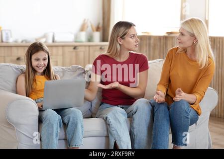 Besorgte Mutter beschwerte sich über Großmutter, dass ihre Tochter einen Laptop benutzte, Inneneinrichtung Stockfoto