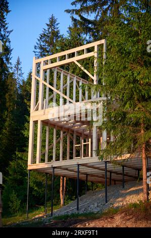 Wohnhaus mit Holzrahmen, das in der Nähe von bewaldeten Flächen errichtet wird. Beginn des Neubauprojekts für gemütliches Haus. Konzept des zeitgenössischen ökologischen Bauens und modernen architektonischen Designs. Stockfoto