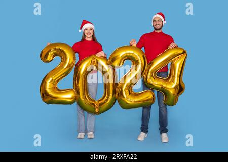 Glückliches Junges Paar In Santa Hats, Das Goldene 2024 Ballons In Den Händen Hält Stockfoto