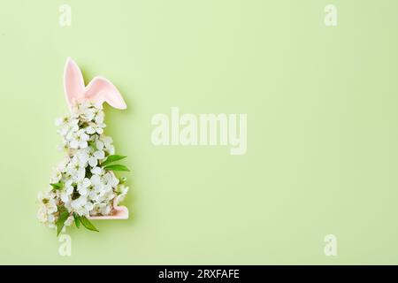 Frohe Ostern. Keramik rosa Form des Osterhasen mit runden Bouquet Quellen frische Kirsch- oder Apfelblüten auf grünem Hintergrund. Osterkarte für den Frühling Stockfoto