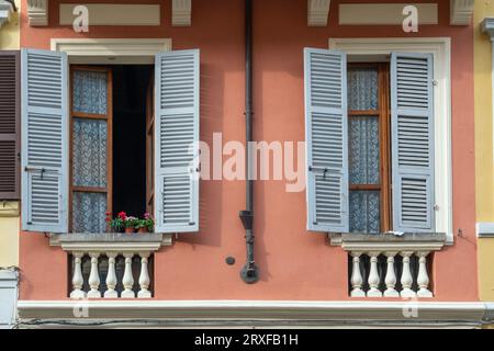 Detail der bunten Fassade eines alten Palastes mit zwei Fenstern, Topfblüten und Holzläden, Parma, Emilia-Romagna, Italien Stockfoto