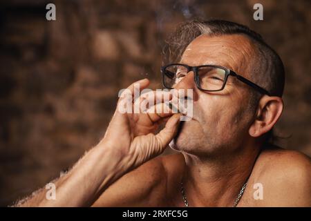 Ein zufriedener älterer Mann, sechzig Jahre alt, raucht nachdenklich. Stockfoto