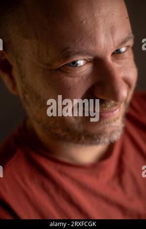 Ein unrasierter Mann in seinen 40ern, der ein freundliches Lächeln und ein durchschnittliches Aussehen hat, wird in einer Nahaufnahme festgehalten Stockfoto
