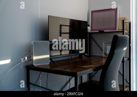 Ecke des Apartments mit Tisch, auf dem sich Fernseher, WLAN-Router, Regale und Computerstuhl befinden; Stockfoto