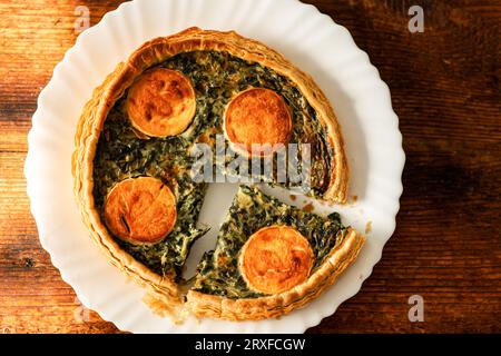 Eine köstliche runde Quiche mit Käse und Spinat, frisch zubereitet und auf einem hölzernen Hintergrund präsentiert, eine erstklassige Wahl für Vegetarier Stockfoto