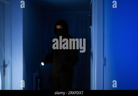 Maskierter Räuber mit Taschenlampe Taschenlampe Überprüfung Wohnung. Stockfoto