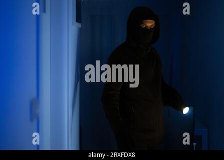 Maskierter Räuber mit Taschenlampe Taschenlampe Überprüfung Wohnung. Stockfoto