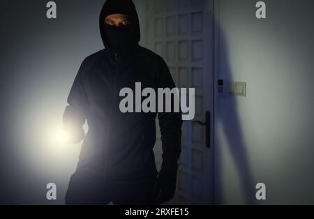 Maskierter Räuber mit Taschenlampe Taschenlampe Überprüfung Wohnung. Stockfoto