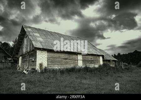 Stillgelegtes altes Gebäude in einem Grasfeld und bewölktem Himmel. Gespuckt. Gruselig. Stockfoto