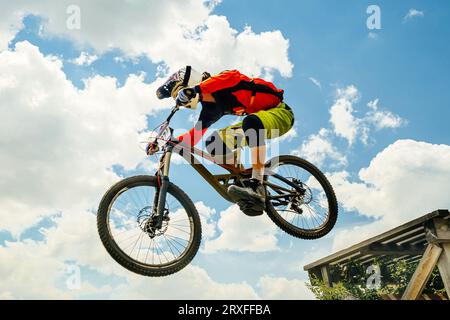 Man-Mountainbiker springen im Flug bergab. Vor dem Hintergrund des blauen Himmels Stockfoto