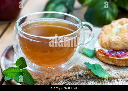Tee in einer Glasschale mit Minzblättern und Croissant auf einem Teller Stockfoto