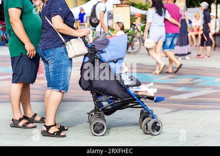 Eltern mit zwei kleinen Kindern in einem Kinderwagen. Zwillinge in einer Kutsche. Frau mit Doppelwagen. Konzeptgeburtenrate von Kindern Stockfoto