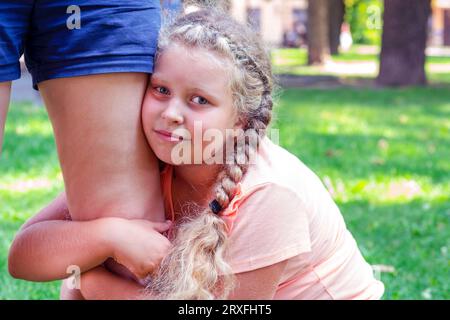 Das Kind umarmt Moms Bein. Porträt eines netten Mädchens, das Mutter hält. Die Liebe des Kindes zu den Eltern. Unglücklicher Teenager. Depressives Mädchen. Düsteres Kind Stockfoto