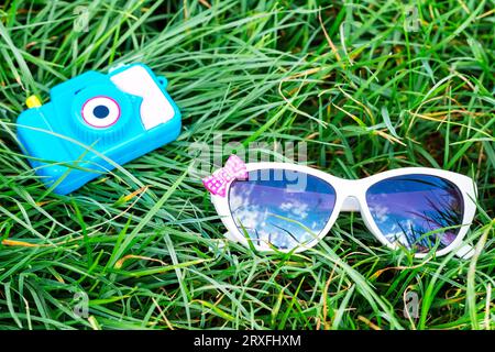 Die Spielzeugkamera und die Kindersonnenbrille auf grünem Gras. Gegenstände für Reisen im Sommer. Konzepturlaub. Ruhe. Picknick. Tourismus Stockfoto