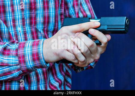 Der Mann mit einer Waffe in den Händen, eine Nahaufnahme. Pistole in den Händen. Der Kriminelle mit der Waffe. Konzeptkriminalität. Es ist bewaffnet und gefährlich. Killer. Zündgerät Stockfoto