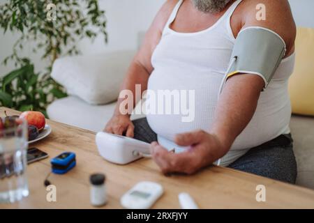 Übergewichtiger Mann, der seinen Blutdruck zu Hause misst. Stockfoto