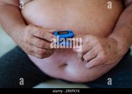 Übergewichtiger Mann, der zu Hause ein Pulsoxymeter zur Messung der Sauerstoffsättigung im Blut einsetzt. Stockfoto