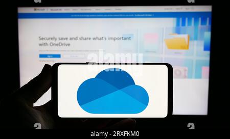 Person, die ein Smartphone mit dem Logo des Datei-Hosting-Dienstes Microsoft OneDrive auf dem Bildschirm vor der Website hält. Konzentrieren Sie sich auf das Display des Telefons. Stockfoto