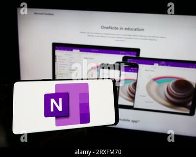 Person, die ein Mobiltelefon mit dem Logo der Notizensoftware Microsoft OneNote auf dem Bildschirm vor der Firmenwebseite hält. Konzentrieren Sie sich auf das Display des Telefons. Stockfoto