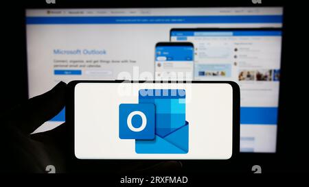 Person, die ein Smartphone mit dem Logo der E-Mail-Software Microsoft Outlook auf dem Bildschirm vor der Website hält. Konzentrieren Sie sich auf das Display des Telefons. Stockfoto