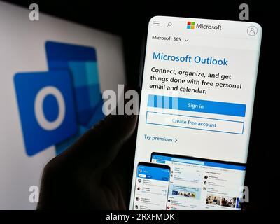 Person, die ein Mobiltelefon mit einer Webseite der E-Mail-Software Microsoft Outlook auf dem Bildschirm vor dem Logo hält. Konzentrieren Sie sich auf die Mitte der Telefonanzeige. Stockfoto
