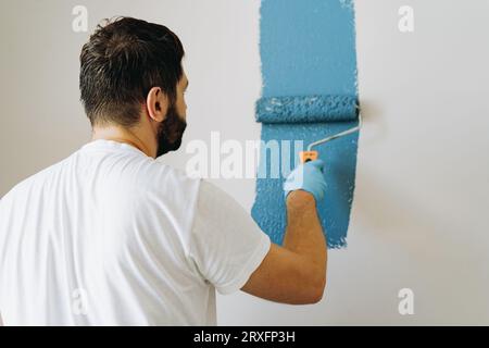 kaukasischer bärtiger Mann malte Wand mit Malerwalze. Malerwohnung, renovierendes Haus mit blauer Farbe. Bild mit selektivem Fokus Stockfoto