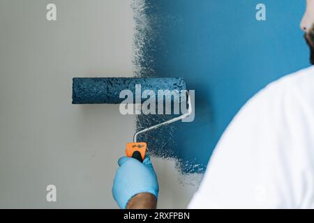kaukasischer bärtiger Mann malte Wand mit Malerwalze. Malerwohnung, renovierendes Haus mit blauer Farbe. Bild mit selektivem Fokus Stockfoto