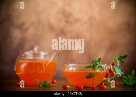 Zubereitetes Getränk aus Reifen Goji-Beeren in einer Glasschale und Teekanne auf einem Holztisch. Stockfoto