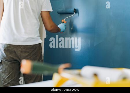 kaukasischer bärtiger Mann malte Wand mit Malerwalze. Malerwohnung, renovierendes Haus mit blauer Farbe. Bild mit selektivem Fokus Stockfoto
