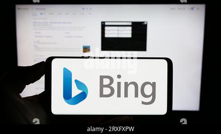 Person, die ein Mobiltelefon mit dem Logo der Websuchmaschine Microsoft Bing auf dem Bildschirm vor der Geschäftswebseite hält. Konzentrieren Sie sich auf das Display des Telefons. Stockfoto