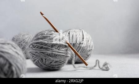 Häkelnadel aus Holz und Kugeln aus grauem Garn zum Häkeln und für Handarbeiten Stockfoto