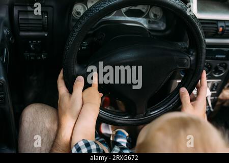 Papa zeigt seinem kleinen Sohn, wie er das Auto fährt, während er hinter dem Steuer sitzt Stockfoto