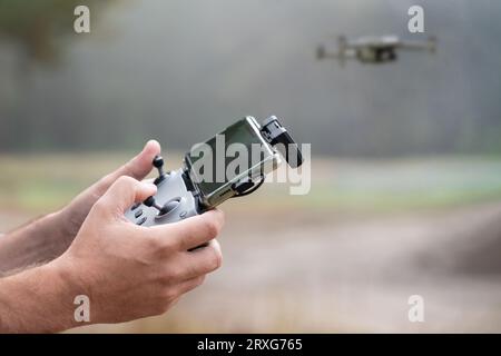 Foto von den Händen des Mannes, die die Fernbedienung einer Drohne halten (Drohnenbediener). Technologiekonzept. Der Mensch hat Spaß mit einem Quadcopter in der Natur. C Stockfoto