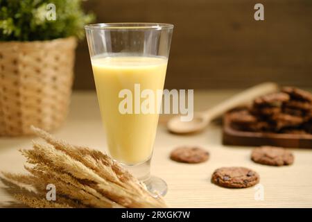 Leckere frische Maismilch im Glas und Maiskolben auf weißem Holztisch. Stockfoto