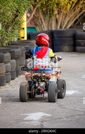 Kleiner Junge fährt ein Motorrad-ATV mit vier Rädern. Outdoor-Aktivität für Kinder auf einem Elektrorennen Quad Bike Maschine. Das Kind Trägt Sicherheitsausrüstung Stockfoto