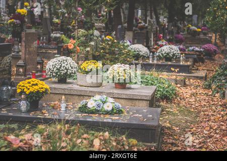 Brennende Kerzen in Laternen, dekorative Verzierungen und Chrysanthemenblüten auf dem Grab auf dem Friedhof Stockfoto