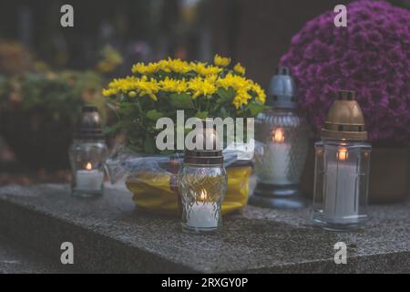 Brennende Kerzen in Laternen, dekorative Verzierungen und Chrysanthemenblüten auf dem Grab auf dem Friedhof Stockfoto