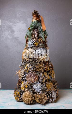 Ein Weihnachtsbaum, der mit eigenen Händen aus vielen Kegeln auf grauem Hintergrund gemacht wurde Stockfoto