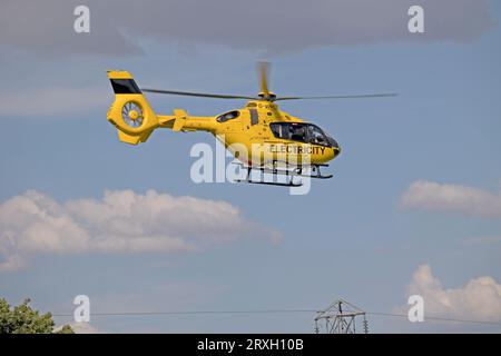 Hellgelber National Grid Elektrizitätshubschrauber im Flug, der Hochspannungsleitungen in der Nähe von Mickleton Chipping Campden UK überprüft Stockfoto