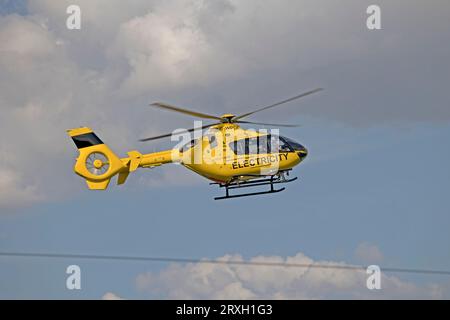 Hellgelber National Grid Elektrizitätshubschrauber im Flug, der Hochspannungsleitungen in der Nähe von Mickleton Chipping Campden UK überprüft Stockfoto